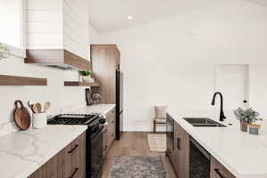 Kitchen with open shelves, modern cabinets, black appliances, light stone countertops, and vaulted ceiling