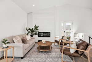 Living area with a high ceiling, a large fireplace, wood finished floors, and recessed lighting