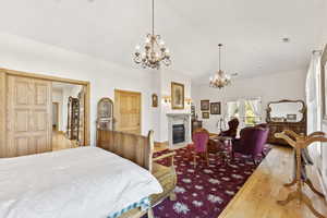 Bedroom with a chandelier, wood finished floors, and a fireplace with flush hearth