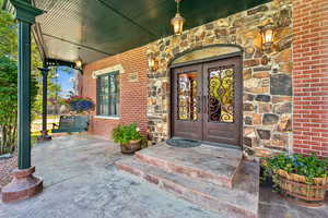 Entrance to property featuring brick siding, stone siding, a porch, and french doors