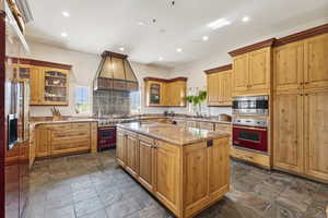 Kitchen with stainless steel appliances, custom exhaust hood, recessed lighting, light stone counters, and a kitchen island with sink