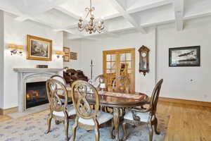 Dining area with coffered ceiling, a chandelier, light wood finished floors, a premium fireplace, and beam ceiling