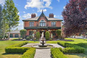 View of front of home featuring a chimney, brick siding, a front lawn, and a balcony
