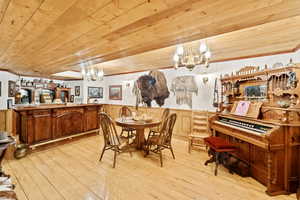 Dining area featuring a chandelier, wainscoting, light wood finished floors, crown molding, and wooden ceiling