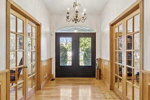 Entrance foyer featuring french doors, wood finished floors, wainscoting, and a chandelier