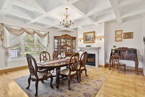 Dining room featuring a chandelier, a fireplace with flush hearth, light wood-style floors, coffered ceiling, and beam ceiling