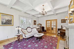 Living area with a chandelier, wood finished floors, coffered ceiling, french doors, and beam ceiling