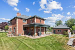 Back of property featuring brick siding, a chimney, a yard, and an outbuilding