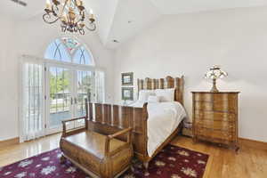 Bedroom featuring access to outside, a chandelier, wood finished floors, french doors, and high vaulted ceiling