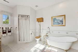 Bathroom featuring tile walls, tile patterned floors, wainscoting, a freestanding tub, and a shower with shower curtain
