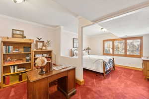 Bedroom with dark colored carpet, crown molding, and a desk
