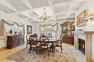 Dining space featuring a chandelier, a fireplace, beam ceiling, coffered ceiling, and light wood finished floors