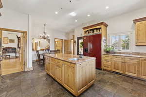 Kitchen with stone tile floors, paneled refrigerator, a kitchen island with sink, light brown cabinets, and recessed lighting