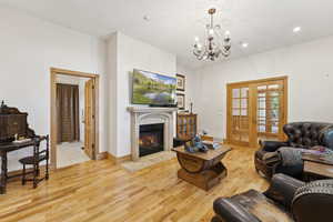 Living area with light wood finished floors, a chandelier, a fireplace with flush hearth, french doors, and recessed lighting