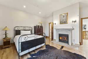 Bedroom featuring wood finished floors, lofted ceiling, a fireplace with flush hearth, and recessed lighting