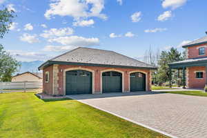 View of side of home with a yard, brick siding, a mountain view, a detached garage, and an outbuilding
