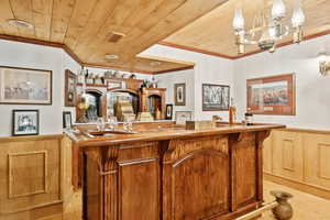 Indoor wet bar featuring wainscoting, wooden walls, ornamental molding, wooden ceiling, and brown cabinets