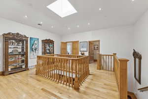 Hallway with an upstairs landing, light wood finished floors, a skylight, and recessed lighting