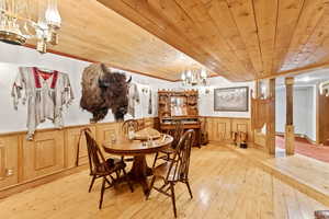 Dining room with a chandelier, a wainscoted wall, hardwood / wood-style flooring, wooden walls, and wooden ceiling