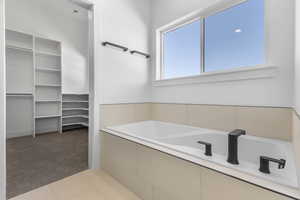 Bathroom with carpet floors, a spacious closet, a bath, and tile patterned flooring