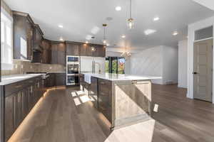 Kitchen with dark brown cabinetry, dark wood-type flooring, decorative light fixtures, a center island with sink, and recessed lighting