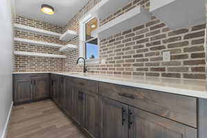 Kitchen with open shelves, dark brown cabinetry, light wood finished floors, and light stone countertops