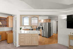 Kitchen with stainless steel appliances, a peninsula, light brown cabinets, light wood-type flooring, and light colored carpet