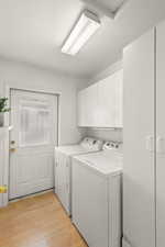 Washroom featuring light wood-style floors, cabinet space, washing machine and clothes dryer, and a textured ceiling