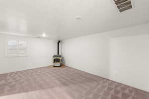 Basement with a wood stove, a textured ceiling, and carpet floors