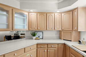 Kitchen with light brown cabinets, light countertops, glass insert cabinets, and recessed lighting
