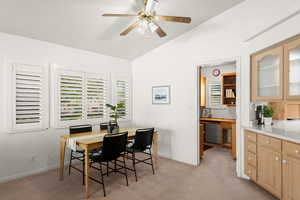 Dining room featuring vaulted ceiling, light colored carpet, ceiling fan, and built in desk