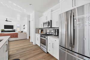 Kitchen featuring stainless steel appliances, white cabinetry, a ceiling fan, open floor plan, and light wood finished floors