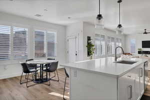 Kitchen featuring light stone countertops, white cabinets, hanging light fixtures, open floor plan, and an island with sink