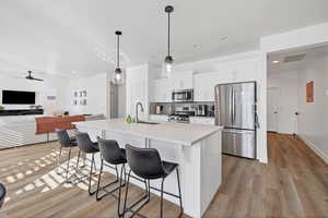 Kitchen with appliances with stainless steel finishes, white cabinets, open floor plan, a breakfast bar, and hanging light fixtures