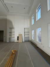 Unfurnished living room featuring a towering ceiling, built in features, and a tray ceiling