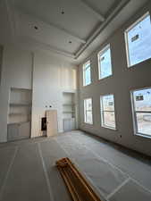 Unfurnished living room featuring built in features, a towering ceiling, and beam ceiling