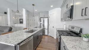 Kitchen with stainless steel appliances, dark wood-style flooring, gray cabinets, light stone countertops, and recessed lighting