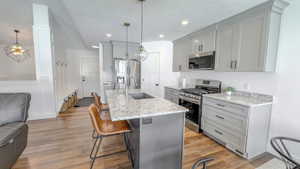 Kitchen with gray cabinets, stainless steel appliances, light stone countertops, a kitchen island with sink, and a textured ceiling