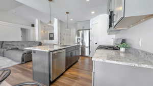 Kitchen featuring light stone countertops, stainless steel appliances, light wood-style floors, open floor plan, and a kitchen island with sink