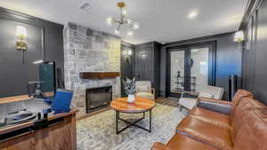 Living area with a stone fireplace, ornamental molding, wood finished floors, french doors, and a chandelier