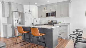 Kitchen featuring gray cabinets, stainless steel appliances, light stone counters, light wood-type flooring, and a kitchen bar