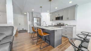 Kitchen with gray cabinetry, light stone countertops, a kitchen breakfast bar, decorative light fixtures, and recessed lighting