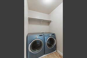 Laundry area featuring light wood-type flooring, a textured ceiling, and washer and dryer