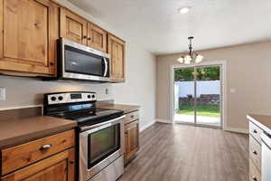 Kitchen with stainless steel appliances, decorative light fixtures, dark wood-style flooring, dark countertops, and a textured ceiling