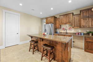 Kitchen with a breakfast bar area, light stone counters, high end fridge, brown cabinetry, and a center island