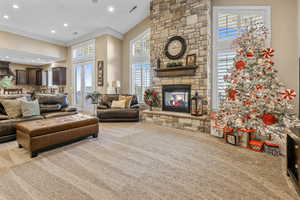Living room featuring a towering ceiling, a stone fireplace, crown molding, light carpet, and recessed lighting