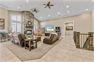 Living room featuring a stone fireplace, ceiling fan, high vaulted ceiling, recessed lighting, and ornamental molding