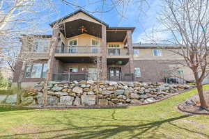 Rear view of house featuring brick siding, stucco siding, ceiling fan, and a lawn