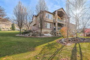 Back of house with brick siding, a lawn, stucco siding, and a balcony