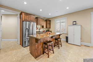 Kitchen with a breakfast bar area, stainless steel refrigerator with ice dispenser, dark stone counters, a kitchen island, and brown cabinetry